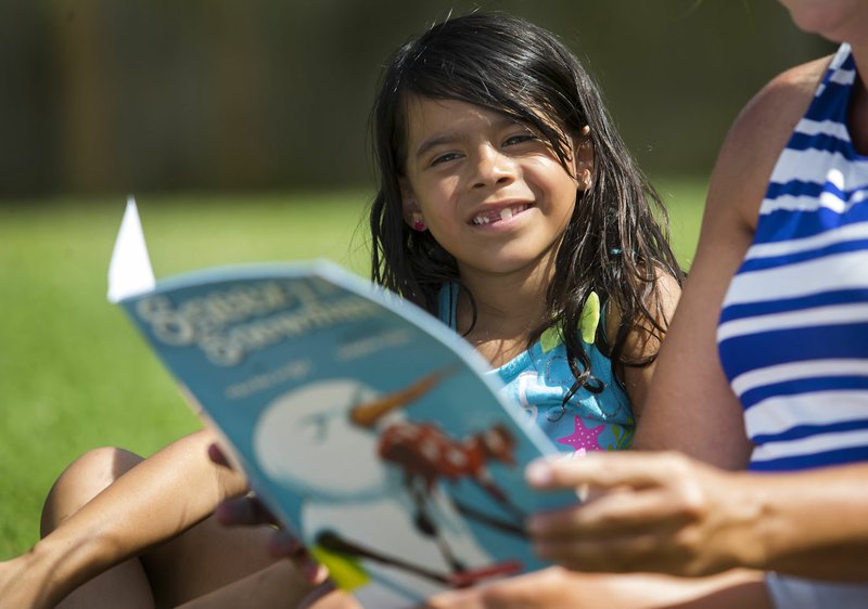 NWA Democrat-Gazette/JASON IVESTER Breetany Garcia, 6, listens as Janelle Miller reads Sneezy the Snowman last month at the Montecito Springs apartment complex in Springdale. Miller and instructional assistant Pam Sweeney brought the mobile library of Sonora Elementary School to the area where many of the school's students live.