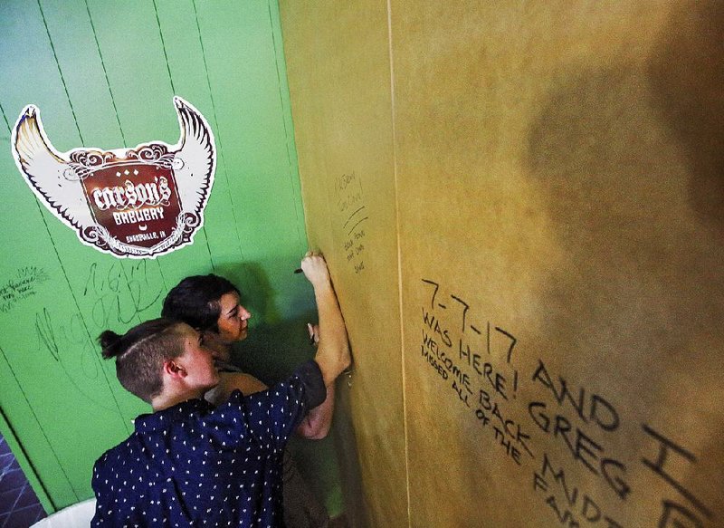 Levi Coffman (left) and Larissa Gudino, both of North Little Rock, leave messages on the wall during Friday’s grand reopening of Midtown Billiards in Little Rock. The popular bar had been closed since a September fire.
