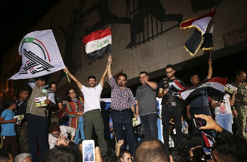 Iraqis celebrate while holding national fl ags in Tahrir square Monday in Baghdad.