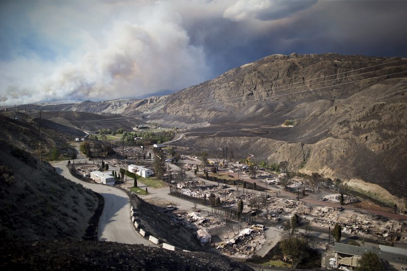 The remains of mobile homes destroyed by a wildfire are seen in Boston Flats as a fire burns on a mountain near Ashcroft, British Columbia, Sunday, July 9, 2017. Wildfires barreled across the baking landscape of the western U.S. and Canada, destroying a smattering of homes and forcing thousands to flee. (Darryl Dyck/The Canadian Press via AP)
