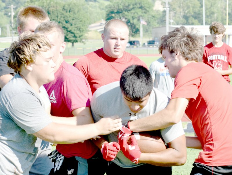 Photo by Rick Peck Tanner Harnar (left) and Bucky Harrell try to knock the ball out of the hands of running back Isrrael De Santiago during a two-week varsity football camp at McDonald County High School that began on July 10.