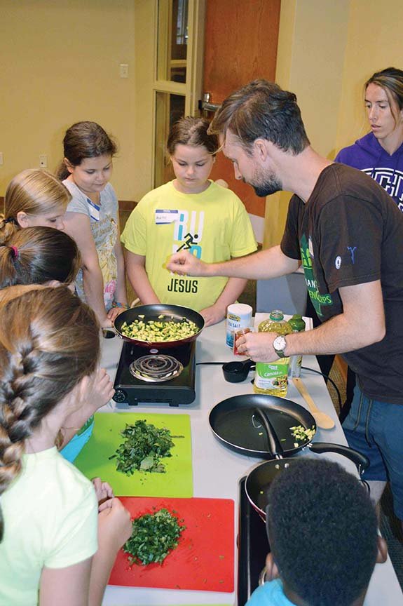 Austin Yockey, adds spices to zucchini in the Cooking Matters! class at the Faulkner County Library in Conway. Also pictured to his right is University of Central Arkansas student Dayna Mounie, who volunteers with the Faulkner County Urban Farm Project at the library, and, from left, students Sydney Lunsford, 10, partially hidden, and 10-year-old twins Ally and Audrey Van Evera, all of Conway.