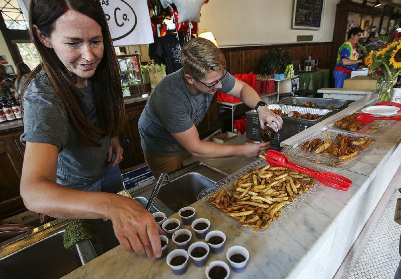 Carol Ann Crowley and Mark Tanner fill sample cups with artisan ketchup Saturday at The Green Corner Store in Little Rock during the launch party for Arkansas Ketchup Co. The company is one of many in the state that focuses on using Arkansas-grown ingredients. 