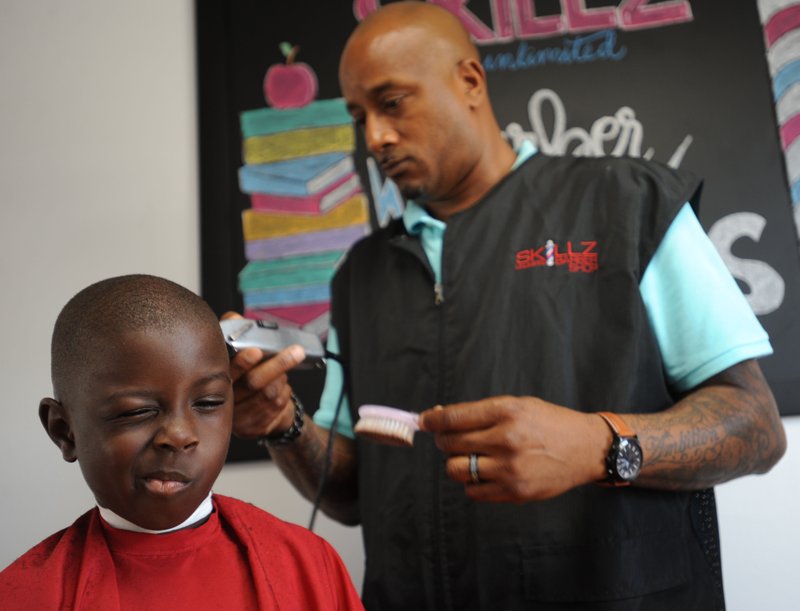 NWA Democrat-Gazette/ANDY SHUPE Kedrick Green, 7, of Springdale reacts to the tickle of the clippers as he has his hair cut by Phillip Mason, owner of Skillz Unlimited Barber Shop, in the kids' reading room in his barber shop in Springdale. The Barbershop Books room features a kid-sized barber chair as well as books and several chairs for sitting and reading.