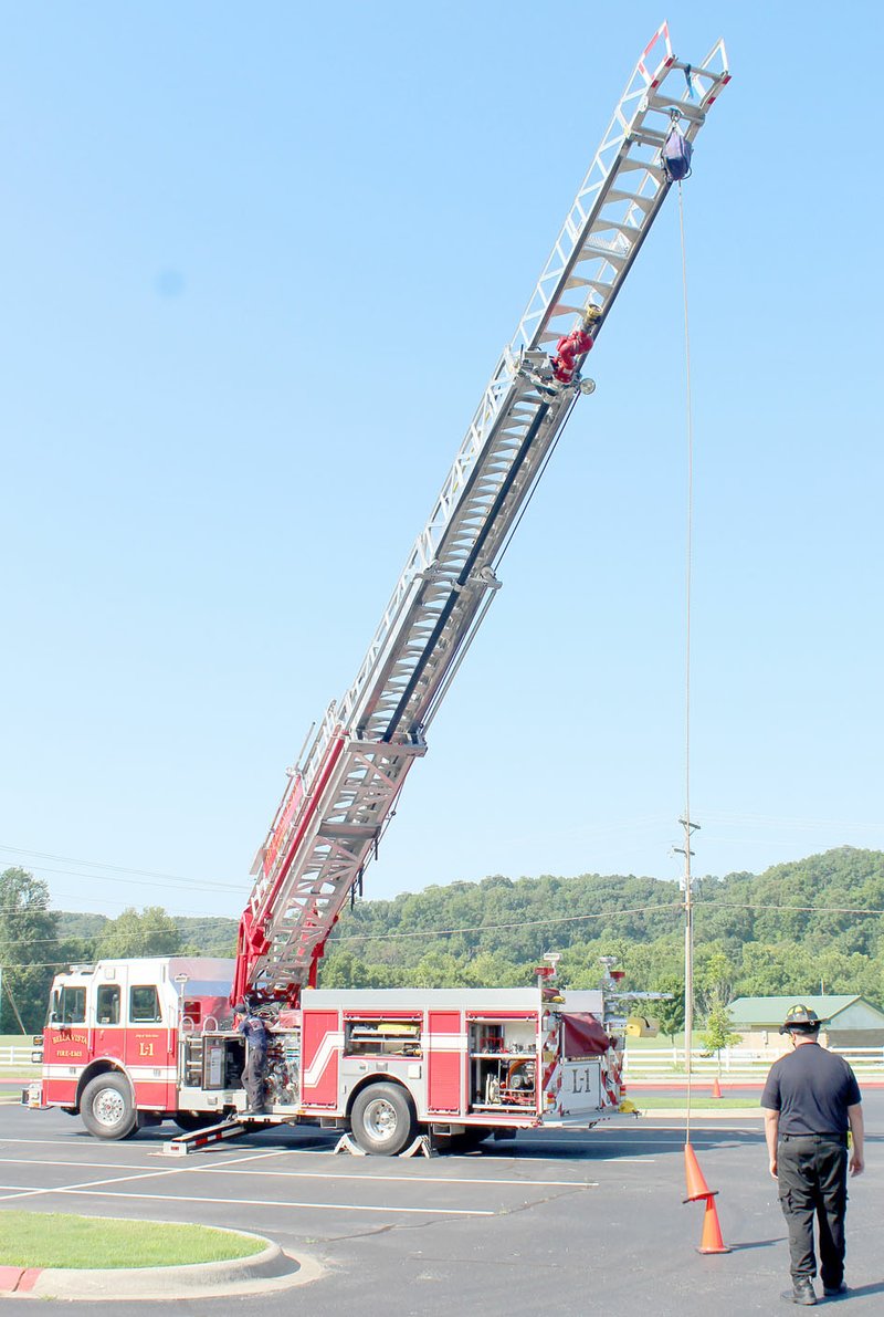 Keith Bryant/The Weekly Vista Firefighter-EMT Aaron Morgan, left, standing on the ladder truck, operates the truck&#8217;s extendable ladder and practices precision movement by attempting to stack cones while firefighter-EMT Ryan Carr directs him. The firefighters practiced July 7 in the Cooper Elementary School parking lot.