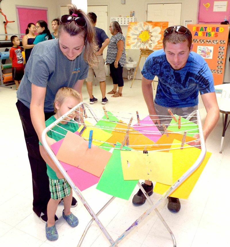 Photo by Randy Moll Katie Chamberlain, with Jeremy Lowery and son Cylas, 4, look at children&#8217;s artwork at the Head Start center in Gentry on July 11. The center held an art show for parents and visitors.