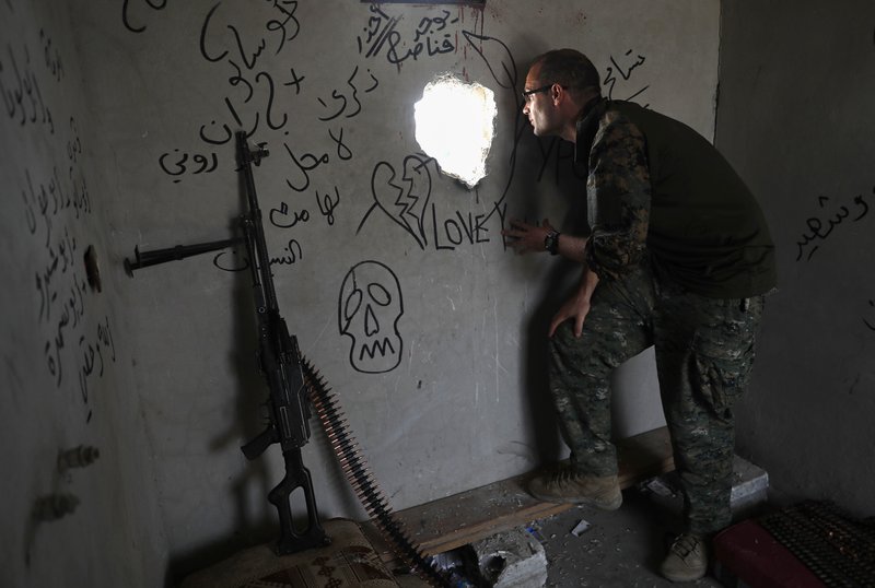 In this Monday, July 17, 2017 photo, Macer Gifford, a 30-year former City broker in London, who fights with an Assyrian militia, that is part of the U.S-backed forces battling Islamic State group militants, looks through a hole into a street controlled by the IS, on the western side of Raqqa, northeast Syria. Several U.S. and British volunteer fighters are on the front lines in the decisive battle against IS for the Syrian city of Raqqa. They joined the U.S.-allied militias in Syria for different reasons, some motivated by testimonies of survivors of the unimaginable brutality that IS flaunted in establishing its self-proclaimed caliphate. (AP Photo/Hussein Malla)