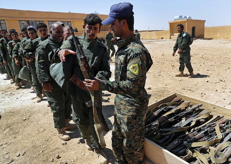 New Syrian troops receive weapons Thursday during a graduation ceremony at Ain Issa desert base in Raqqa province. Some 250 residents of the province are the latest to graduate from a U.S.-training course, after which they will help secure areas captured from Islamic State militants. 