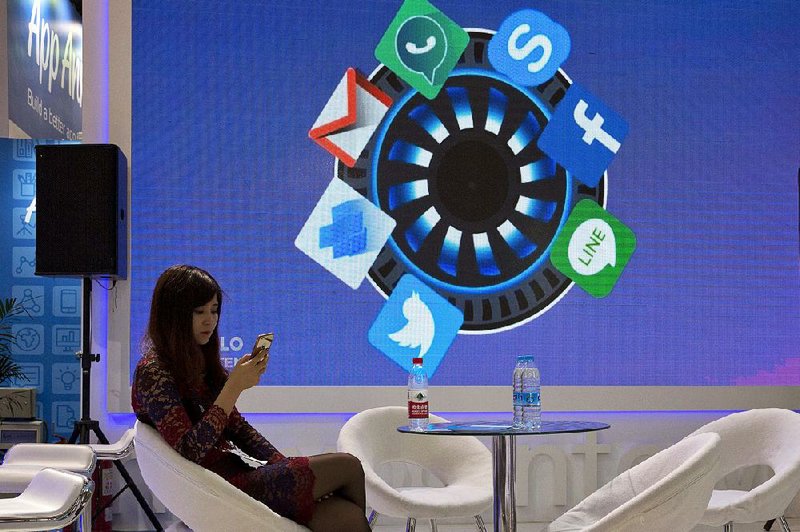 A woman at the Global Mobile Internet Conference in Beijing in April checks her phone near icons of apps that are mostly banned in China.
