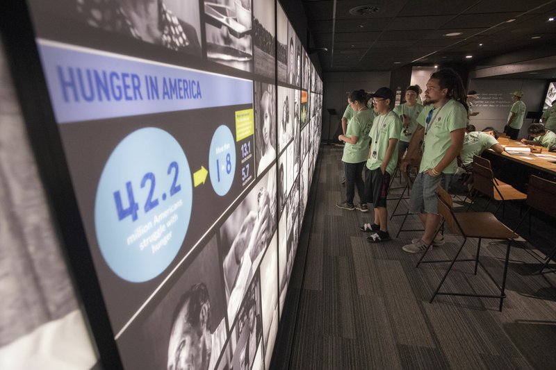 A group of students looks at an exhibit on hunger Saturday at the Fayetteville Farmers’ Market. The exhibit is from MAZON, a national advocacy organization inspired by Jewish values and ideals that is working to end hunger across the United States and Israel. The exhibit is housed inside a 53-foot-long big rig and is designed as a 45-minute experience for 30 guests at a time. The exhibit will be at the Fayetteville square through Wednesday. Visitors need to make a reservation through the website thisishunger.org.