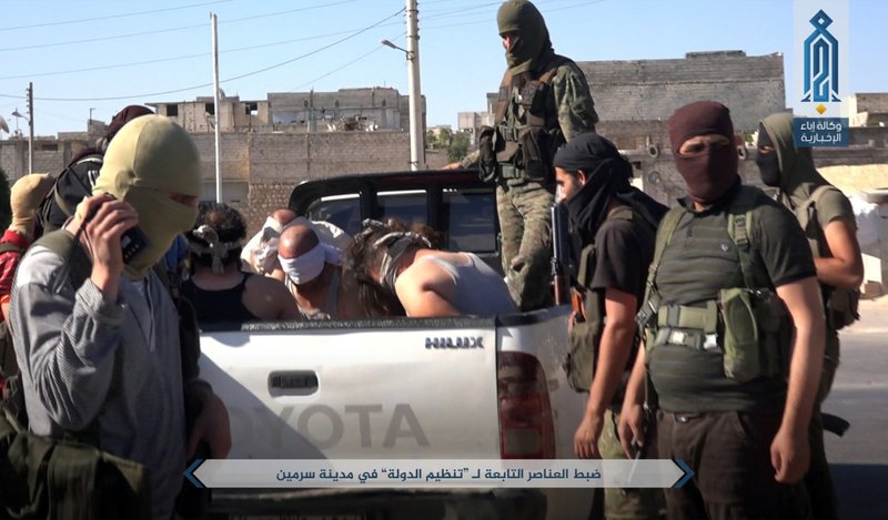 This Sunday, July 9, 2017 photo, released by Ibaa news agency, the communications arm of the al Qaeda-linked Levant Liberation Committee, outlet that is consistent with independent AP reporting, shows al-Qaida-linked fighters after they detained alleged members of the Islamic State group in the northwestern Syrian village of Sarmin in Idlib province.  (Ibaa News Agency, via AP)