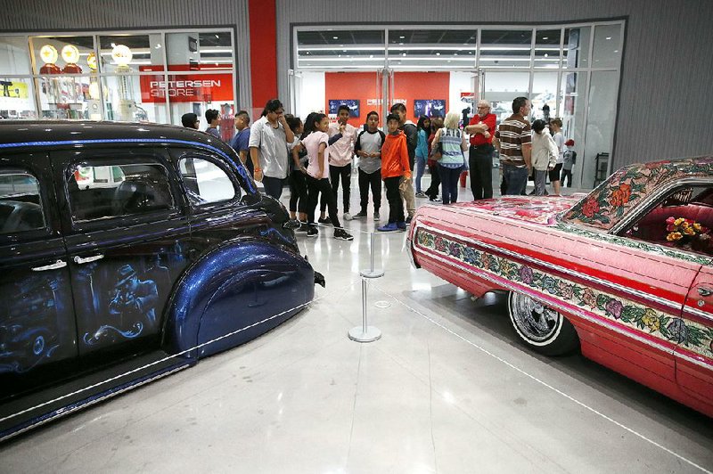 Visitors examine a 1939 Chevrolet Master Deluxe named Gangster Squad ’39, (left) and Jesse Valadez’s Gypsy Rose, a customized 1964 Chevrolet Impala, during “The High Art of Riding Low” at the Petersen Automotive Museum in Los Angeles. The exhibition showcases lowrider-inspired fine art.