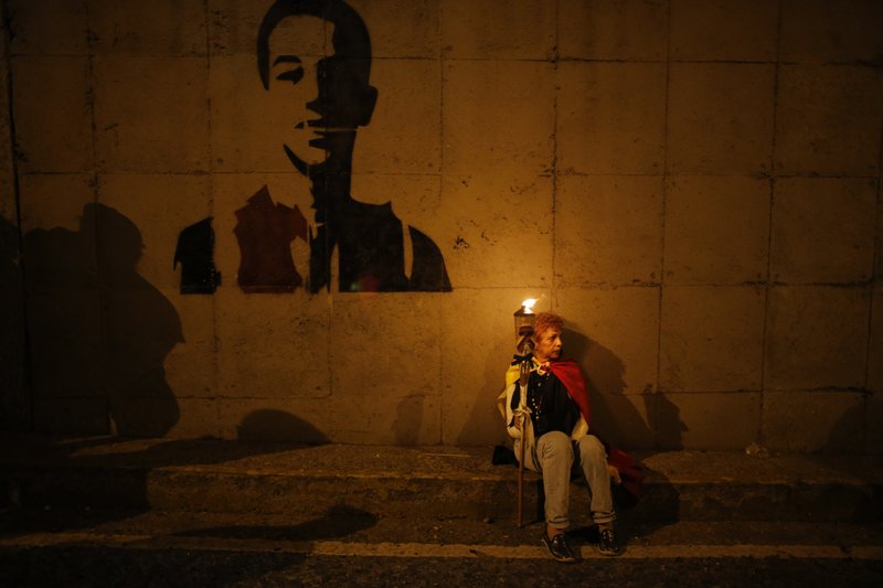 FILE - In this June 8, 2017 file photo, a woman takes part in a vigil near a stenciled image of anti-government protester Neomar Lander near the site where he died, in Caracas, Venezuela.  (AP Photo/Ariana Cubillos, File)