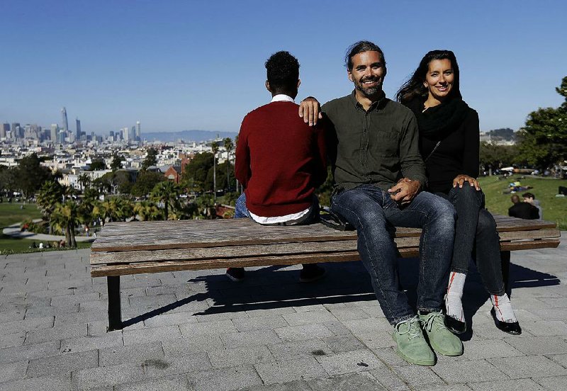 Mike Gougherty (center) and Julie Rajagopal pose for photos with their 16-year-old foster child from Eritrea at Dolores Park in San Francisco. When their foster child landed in March, he was among  the last refugee foster children to make it into the U.S.