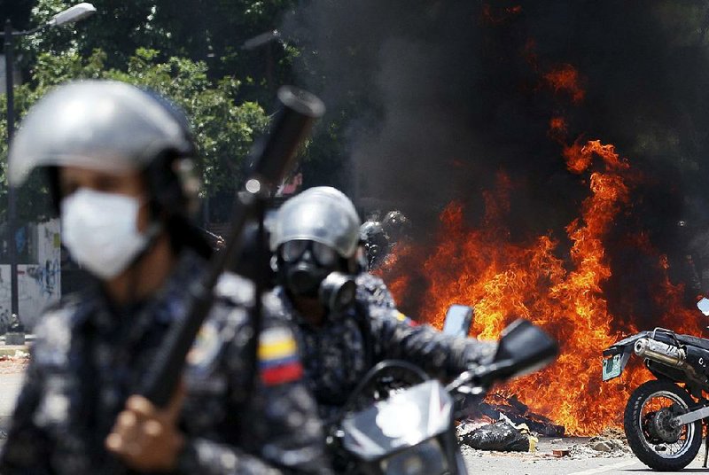 Venezuelan national police move away from the flames after an explosion at Altamira Square during clashes with anti-government demonstrators Sunday in Caracas, Venezuela.