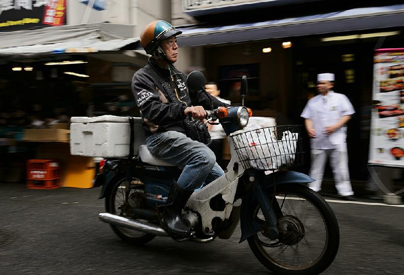A man rides a Honda Super Cub motorcycle at Tsukiji Market in Tokyo in June. Honda, Yamaha Motor Co. and Suzuki Motor Corp. are retiring most of their 50cc scooter models this year and warning they may phase them out altogether as environmental compliance costs make them unprofitable.