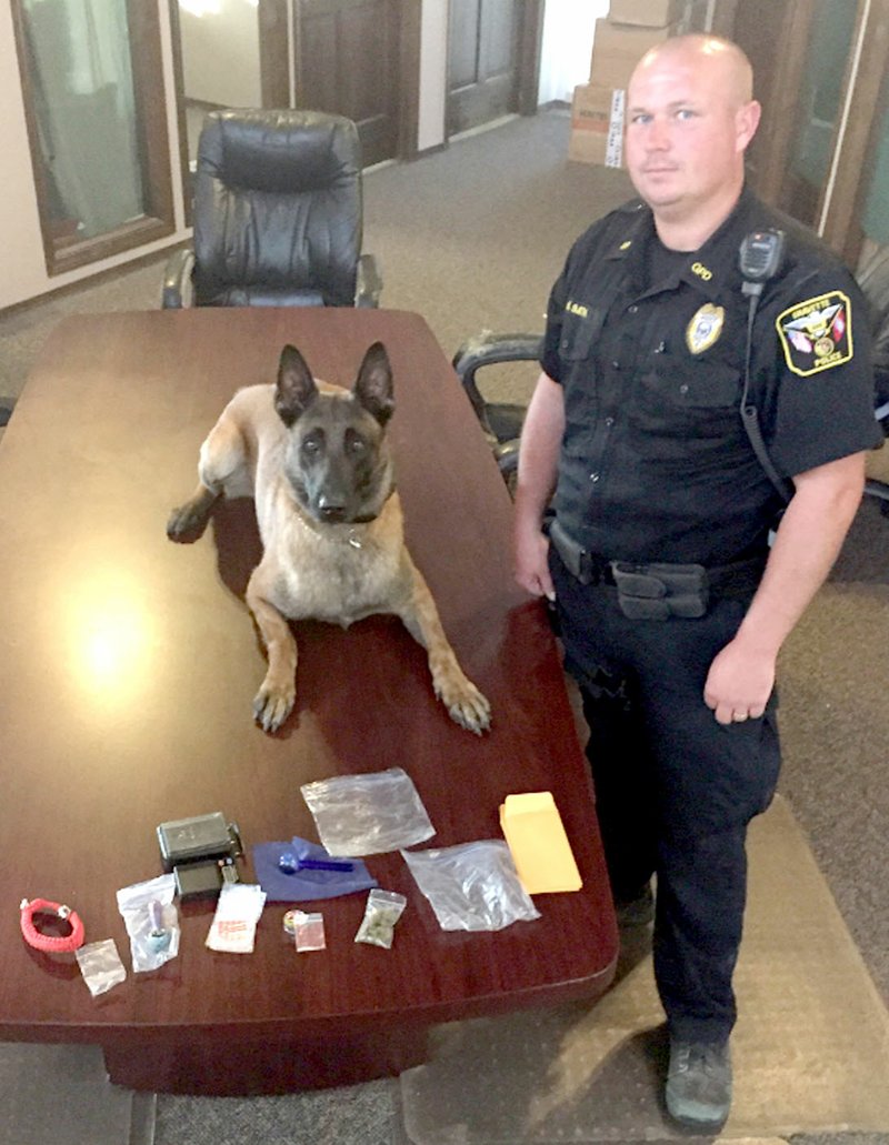Submitted Photo Officer Bryan Smith, of the Gravette Police Department, and the department&#8217;s canine officer, K-9 IKKS, posed with items of drug paraphernalia recovered from a vehicle during a routine traffic stop Monday, July 24. Chuck Skaggs, Gravette chief of police, praised Smith and IKKS for their tireless efforts to keep the Gravette community drug-free.