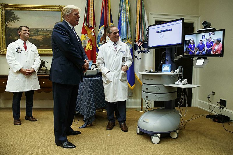 Veterans Affairs Secretary David Shulkin stands with President Donald Trump as Trump talks via technology with a patient during a Veterans Affairs Department “telehealth” event Thursday at the White House. Trump on Thursday criticized Congress over sanctions against Russia and the failure to repeal and replace the 2010 health care law.