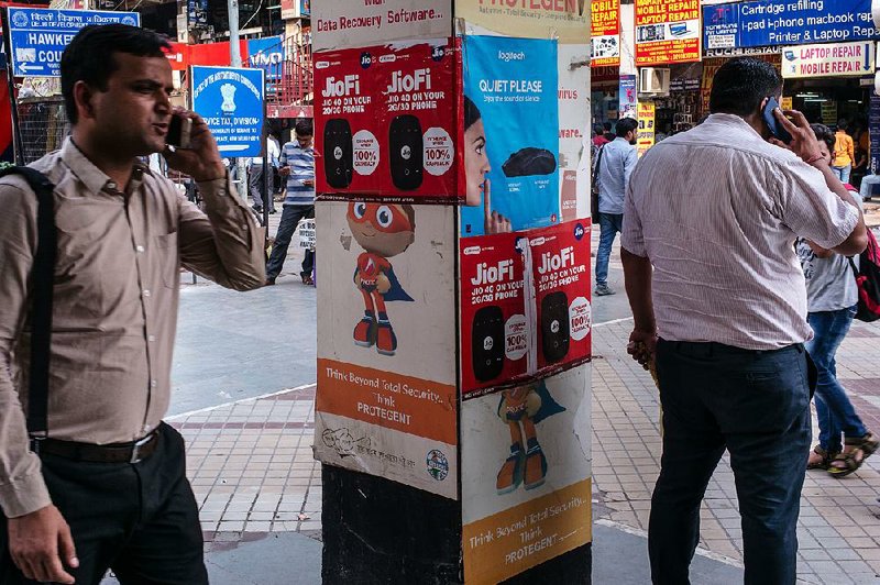 Pedestrians use smartphones near advertising for the Jio mobile network at the Nehru Place IT Market in New Delhi in May.