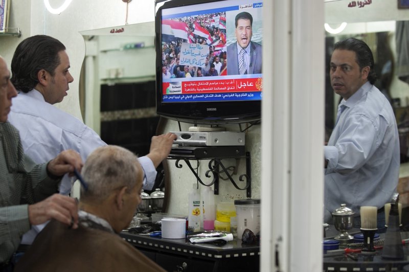 FILE - In this May 4, 2011 file photo, a Palestinian barber gives a customer a haircut as a TV set shows a demonstration in Egypt, on the Al Jazeera channel, at a barber shop in Jerusalem's Old city. 