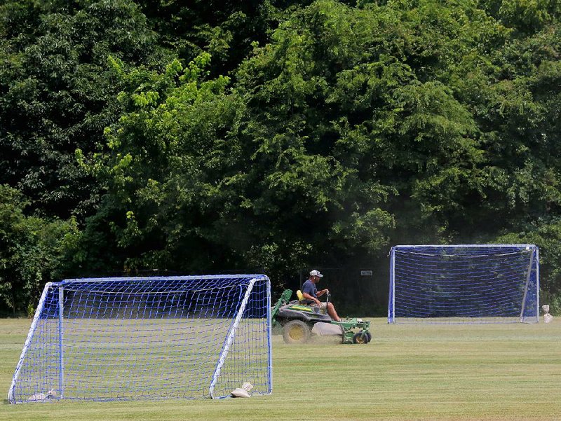 FILE - A man and his mower trim the grass on soccer fields at Little Rock's Murray Park.