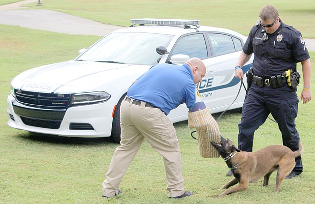Keith Bryant/The Weekly Vista Officer Justin Green, left, wears a protective sleeve for police dog Cabo to practice biting when commanded by K9 officer Travis Trammell.