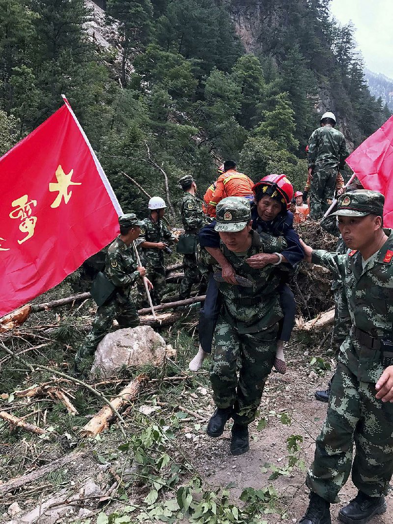 A paramilitary policeman on Wednesday carries a woman over a road damaged by an earthquake in Jiuzhaigou county in southwestern China’s Sichuan province.