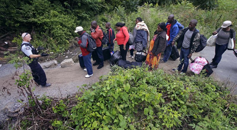 A Royal Canadian Mounted Police officer, left, standing in Saint-Bernard-de-Lacolle, Quebec, advises migrants that they are about to illegally cross from Champlain, N.Y., and will be arrested, Monday, Aug. 7, 2017. Officials on both sides of the border first began to notice last fall, around the time of the U.S. presidential election, that more people were crossing at Roxham Road. Since then the numbers have continued to climb. (AP Photo/Charles Krupa)