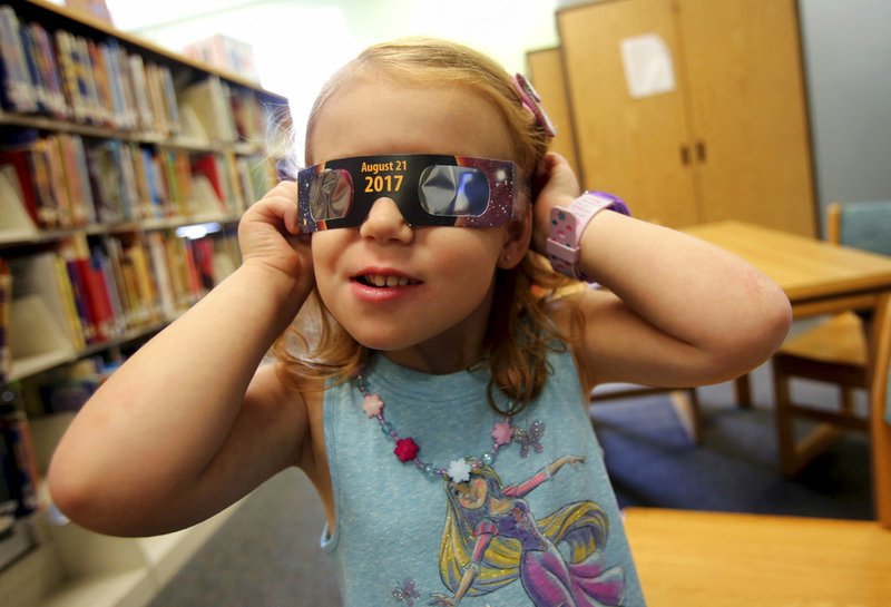 In this Wednesday, Aug. 2, 2017 file photo, Emmalyn Johnson, 3, tries on her free pair of eclipse glasses at Mauney Memorial Library in Kings Mountain, N.C. Glasses are being given away at the library for free while supplies last ahead of the big event on Aug. 21. 
