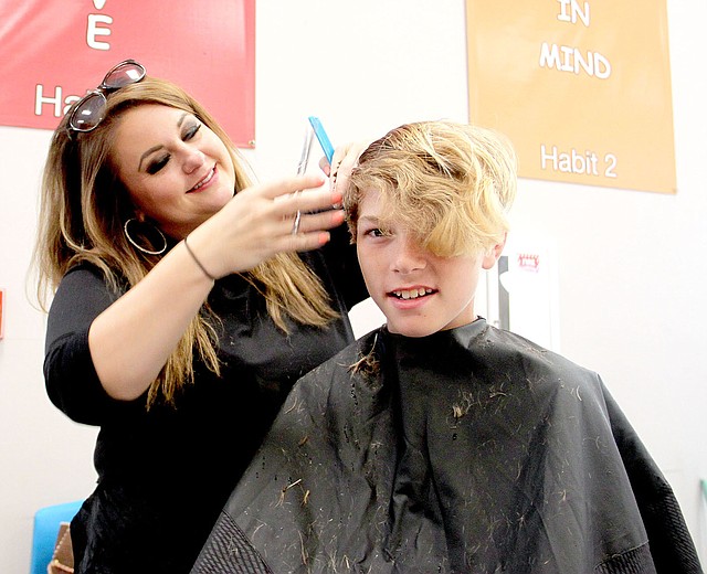 PHOTOS BY LYNN KUTTER ENTERPRISE-LEADER Amber Daniels with Only Prettier Salon in Farmington gives a free haircut to Chance Walker, 13, of Lincoln. About eight hairstylists from the area donated their time at the Lincoln Back to School Bonanza.