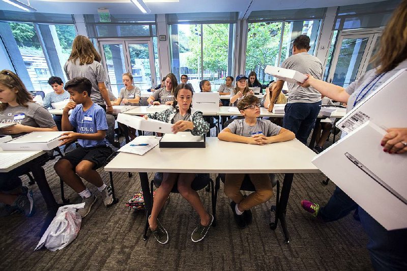 Thaden School seventh-graders Ella Wise (left) looks at her computer as Ben Jones watches teachers hand out new computers during an orientation Friday in a room at Crystal Bridges museum.