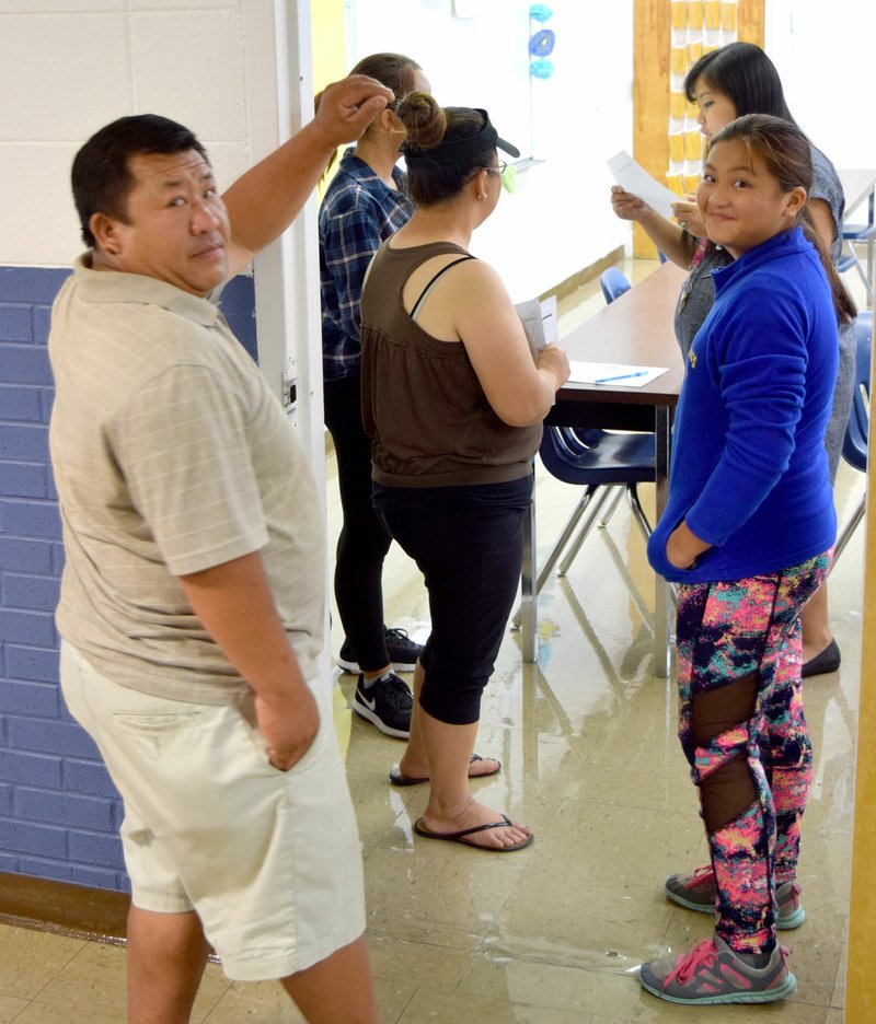 Photo by Mike Eckels Yeng Lee (left) and Lindy Lee (right) wait outside a classroom during the Decatur High School open house Aug. 10 in Decatur. Emme Lee (upper right), with her mother Chia, goes through the registration process with Tang Jones, one of her teachers.