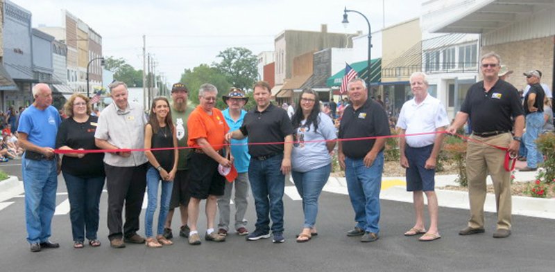Photo by Susan Holland Gravette mayor Kurt Maddox, center, was joined by state representative Kim Hendren, Justice of the Peace Bob Bland, city council members Melissa Burnett and Ron Theis, city finance director Carl Rabey, Main Street merchants and project contractors as he cut the ribbon for Main Street improvements before the annual Gravette Day parade.