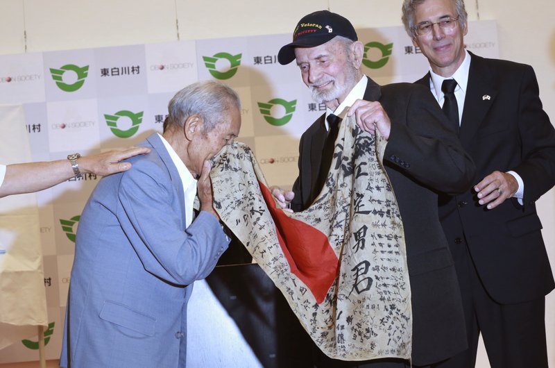 WWII veteran Marvin Strombo, center, returns Tatsuya Yasue, left, a Japanese flag with autographed messages which was owned by his brother Sadao Yasue, who was killed in the Pacific during World Work II, during a ceremony in Higashishirakawa, in central Japan's Gifu prefecture Tuesday, Aug. 15, 2017. Strombo has returned to the fallen soldier's family the calligraphy-covered flag he took from the man's body 73 years ago. (AP Photo/Eugene Hoshiko)