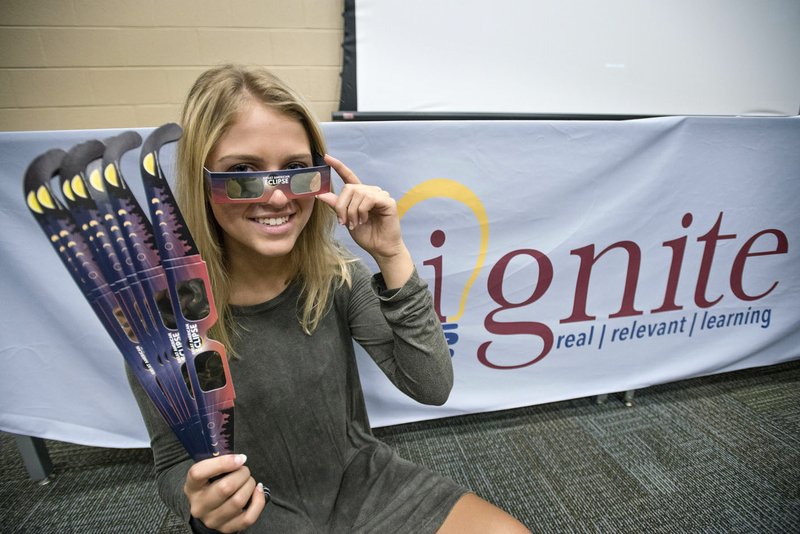 Hailey Brown, a Bentonville High senior, poses with solar eclipse viewing glasses Friday at Bentonville West High in Centerton. Brown, a second-year student in the Bentonville Public Schools Ignite digital design program, designed the graphics on the glasses which will be handed out to students in the district to view the solar eclipse Monday.