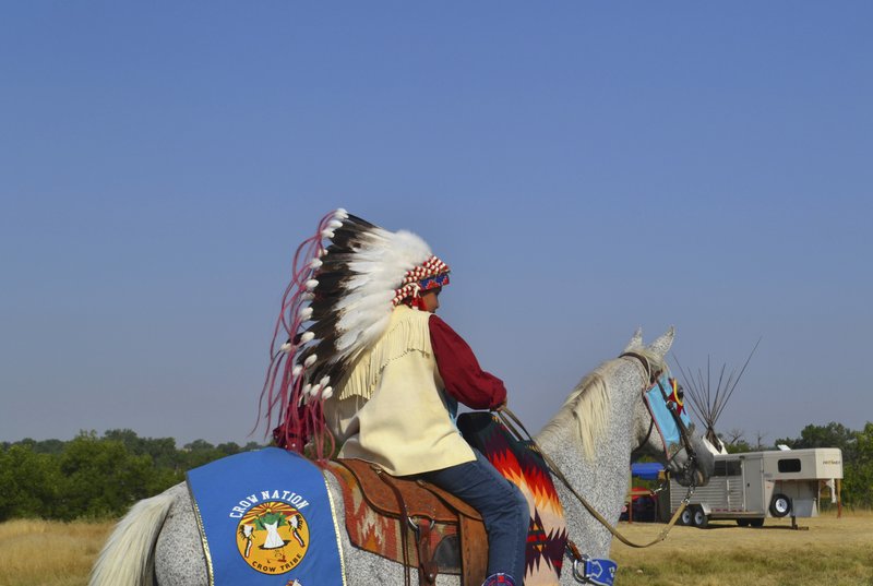 In this Friday, Aug. 18, 2017, photo, a boy wearing a traditional headdress rides through the Crow Fair grounds in Crow Agency, Mont. For the Crow Tribe, the eclipse coincides with the Parade Dance at the annual Crow Fair, marking the tribe's new year. 