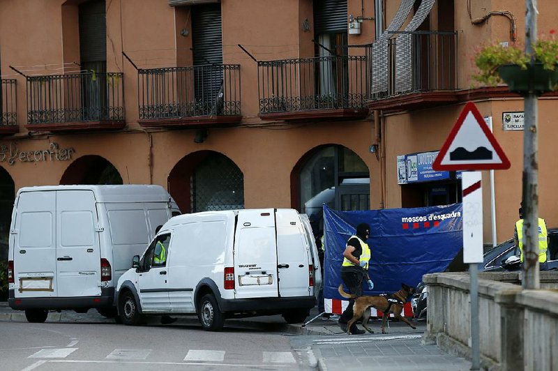 A police officer takes a dog through the entrance of a telephone call center Tuesday in Ripoll in the Pyrenees region of Spain where the suspected driver of the van used to mow down pedestrians Thursday in Barcelona was shot and killed by police Monday.