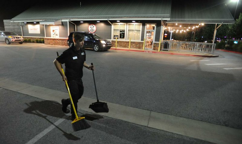 Kirstie Hoelzeman, a shift supervisor at Slim Chickens in Fayetteville, sweeps up litter. The restaurant chain is experimenting with longer hours of operation at its drive-thrus.