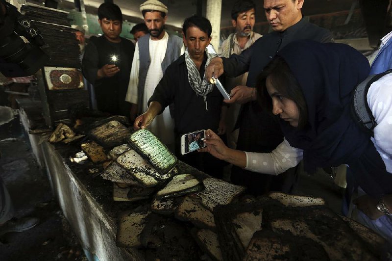 Afghans photograph a burned copy of  the Koran on Saturday  inside  the Shiite mosque  in Kabul where dozens were killed in an attack Friday.
