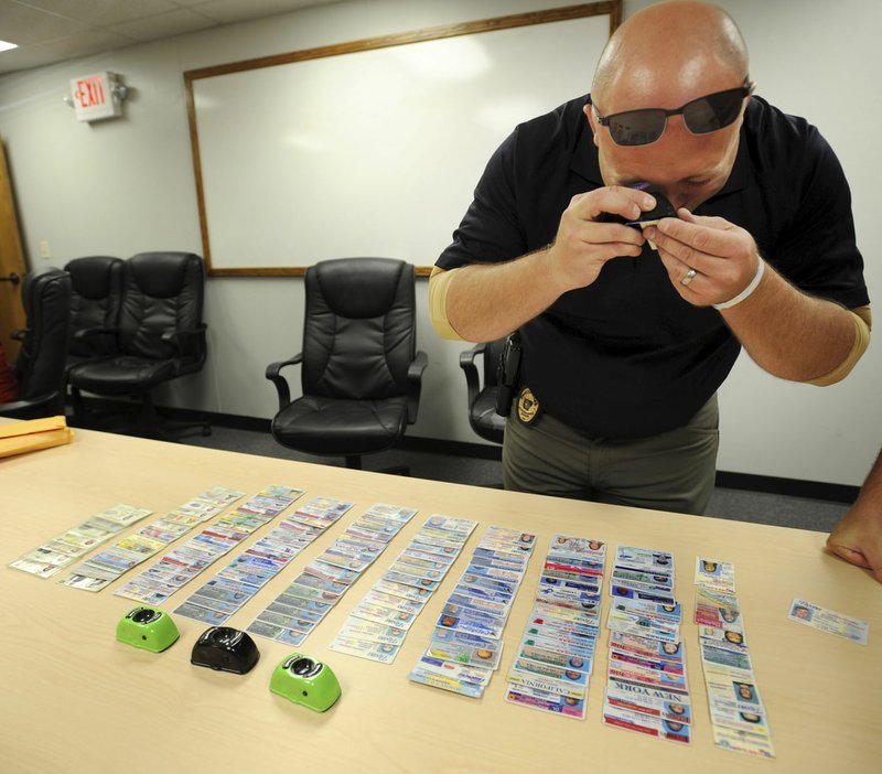 NWA Democrat-Gazette/ANDY SHUPE Cpl. Dallas Brashears of the Fayetteville Police Department uses a specially made device to show printing errors in a fake ID Thursday that was previously confiscated and used for training at the police department.