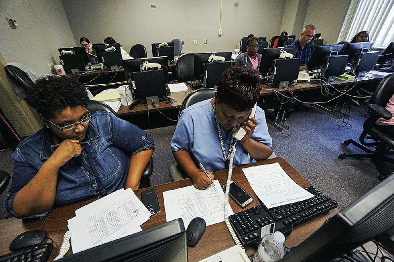 Caregiver Cheryl Thompson (right) takes a call Sunday as sleep technologist Monica Abraham helps her with some information at the John L. McClellan Memorial Veterans Hospital in Little Rock. Both have volunteered to help field calls as the Houston Call Center for Veterans Affairs was shut down because of Harvey.