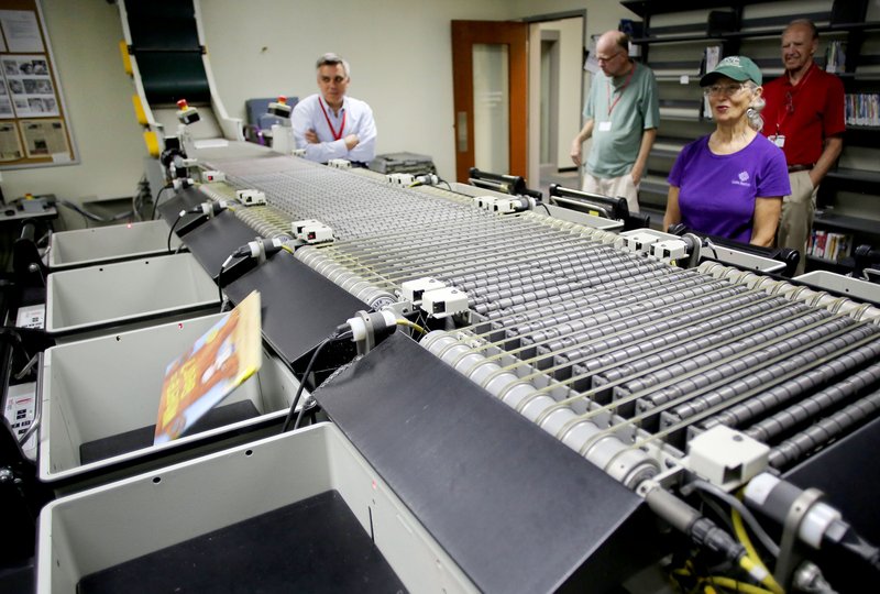 NWA Democrat-Gazette/DAVID GOTTSCHALK Automation in the sorting room handles the 1 million-plus items checked out of the library each year. A 300-foot conveyor belt carries items from the book drops to the sorting room. A radio-frequency identification chip card in each book is read, and the conveyor drops the book into the appropriate bin - fiction, nonfiction, juvenile, movies, audio and more. An employee puts the returned books on carts for each department, which are then pushed to the section and the books reshelved.