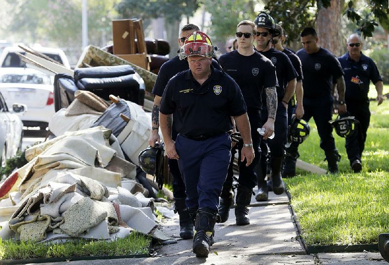 Firefighters pass piles of household debris Thursday in a Houston neighborhood as they conduct a door-to-door survey to see whether any residents have emergency needs. 