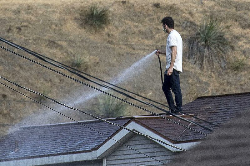 A man trying to protect his house from a spreading wildfire waters down the roof Saturday in the Sun Valley neighborhood north of Los Angeles.