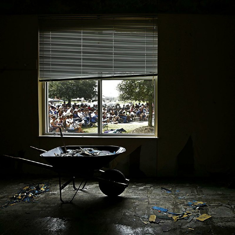People are seen through the window of a water-damaged room as they congregate for a service in the parking lot of First Baptist Church in Humble, Texas.