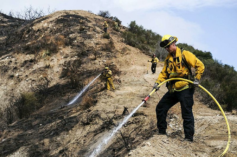 Firefighters on Monday douse hot spots from a wildfire on a hillside near Interstate 210 in the Sunland-Tujunga section of Los Angeles.