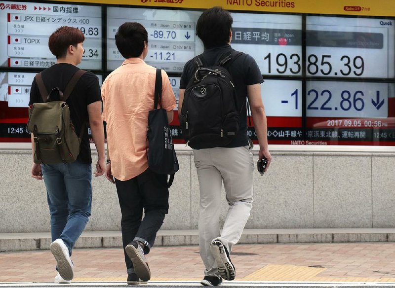 People walk Tuesday near a securities firm in Tokyo where the Nikkei 225 index fell 0.6 percent. International markets were mixed Tuesday as traders dealt with tension on the Korean Peninsula.  