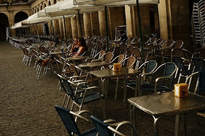 Two women sit outside an empty bar terrace at Plaza de la Constitucion square in Vitoria, Spain, on Monday. The European Central Bank announced Thursday that it was looking to end its bond-buying program next month.