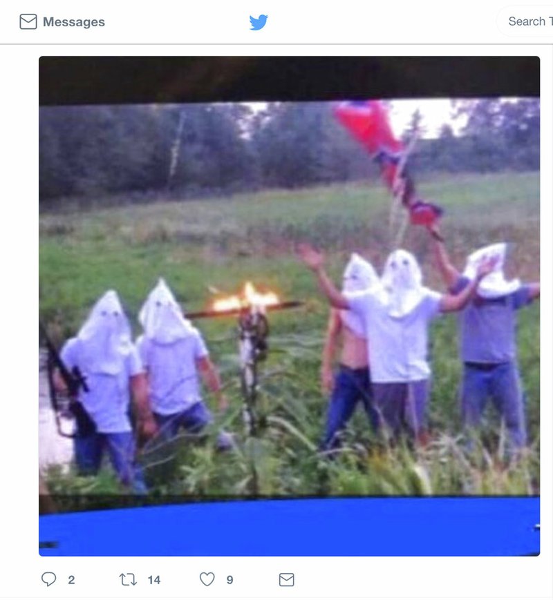 In this screen shot image taken from Twitter, five people wearing white hoods wave a Confederate flag next to a burning cross.