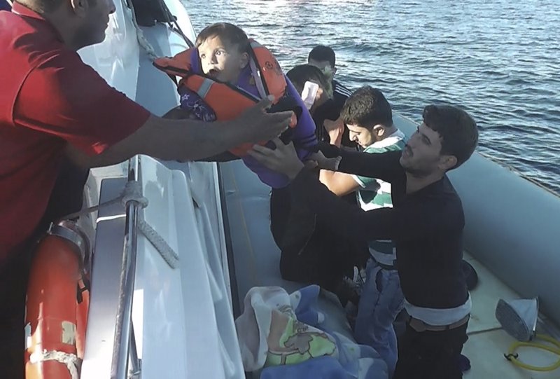 In this Friday, Sept. 8, 2017 video frame grab image, made available by Turkey's Coast Guard Saturday, Sept. 9, 2017, a Syrian migrant among others, lifts a small child onto a Turkey's coastguard vessel from a rubber dinghy, caught while trying to cross to Greece from Turkey's Izmir province. 